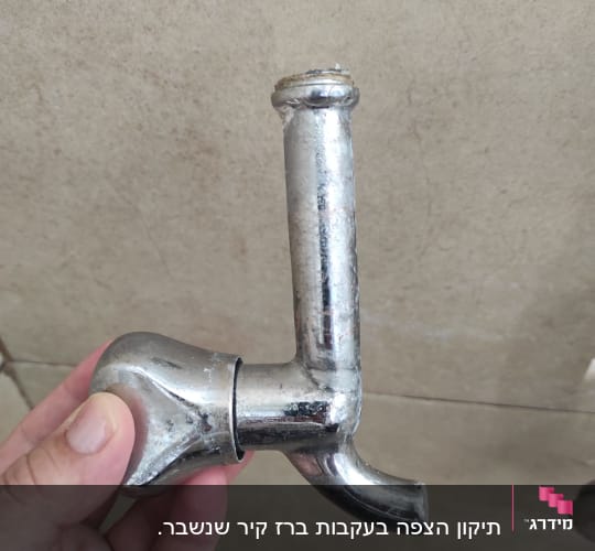 ברז מתכת מוחזק ביד על רקע קיר